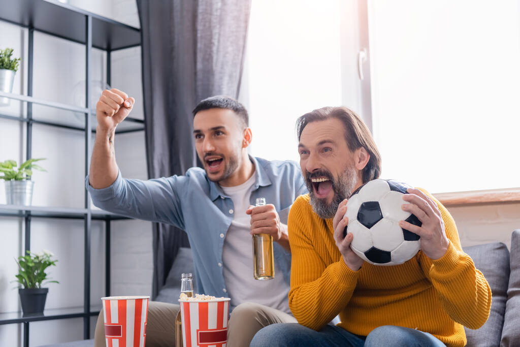 excited man screaming near hispanic son showing win gesture while watching football match at home - Photo, Image