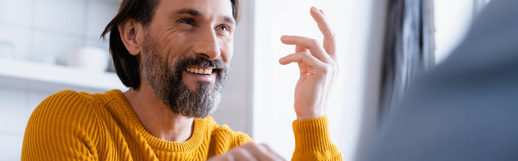 homem barbudo alegre sorrindo e gesticulando em casa em primeiro plano borrado, banner - Foto, Imagem