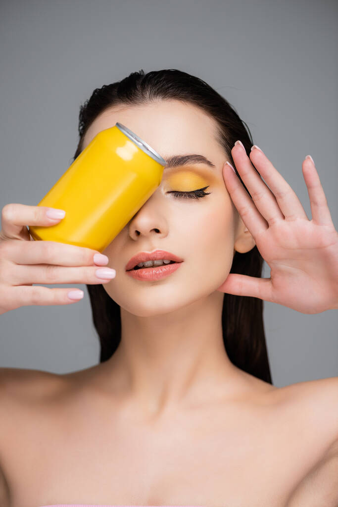 μελαχρινή νεαρή γυναίκα με κλειστά μάτια κρατώντας κίτρινο κουτί με αναψυκτικό που απομονώνεται σε γκρι  - Φωτογραφία, εικόνα