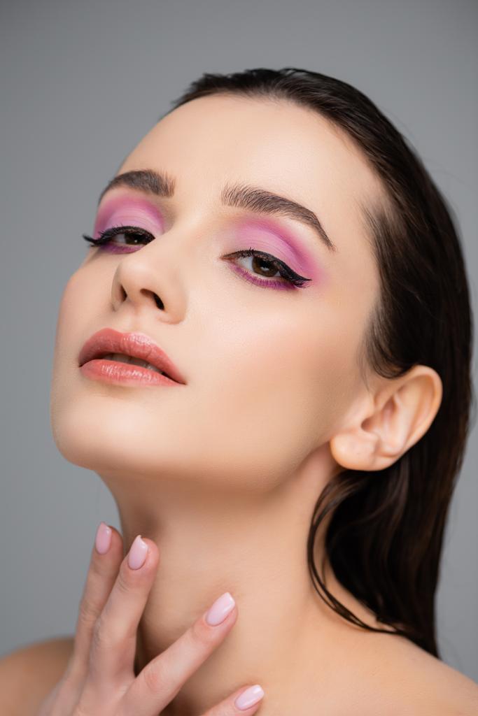 young woman with pink eye shadows and bare shoulders looking at camera isolated on grey  - Photo, Image