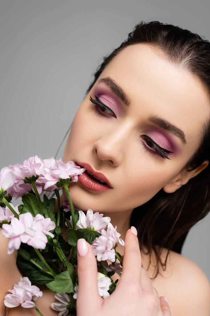 ピンクの目の影をした若い女性が灰色で隔絶された花の近くを  - 写真・画像