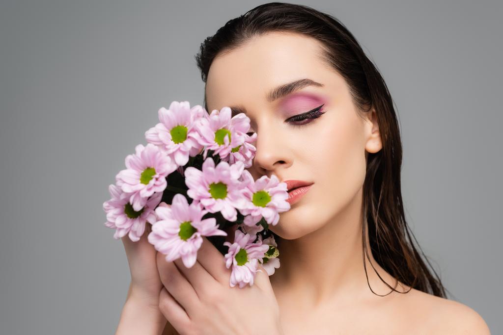 brunette jonge vrouw met roze ogen schaduwen houden bloemen geïsoleerd op grijs  - Foto, afbeelding