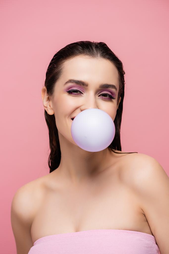 брюнетка жінка з голими плечима дме бульбашкою ізольована на рожевому
 - Фото, зображення