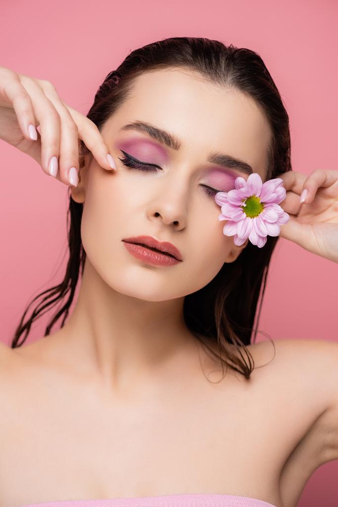 zmysłowa młoda kobieta z zamkniętymi oczami trzymająca kwiat odizolowany na różowo - Zdjęcie, obraz