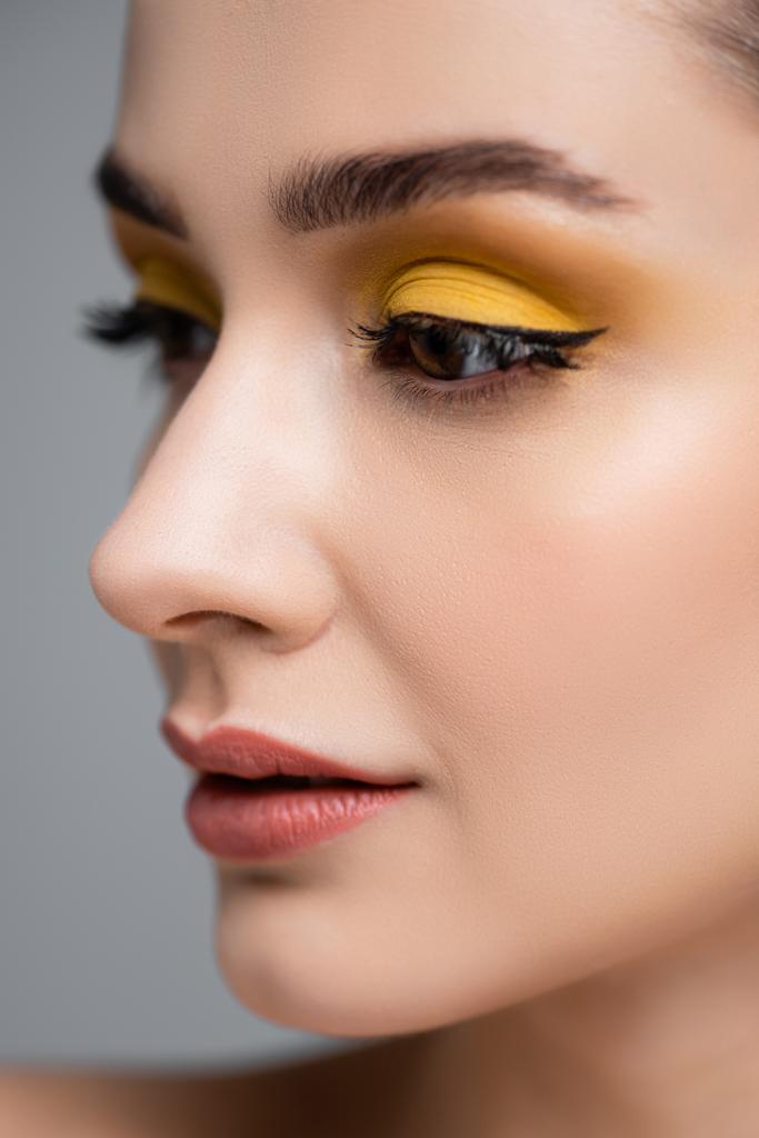 close-up van jonge vrouw met gele oogschaduw weg te kijken geïsoleerd op grijs - Foto, afbeelding