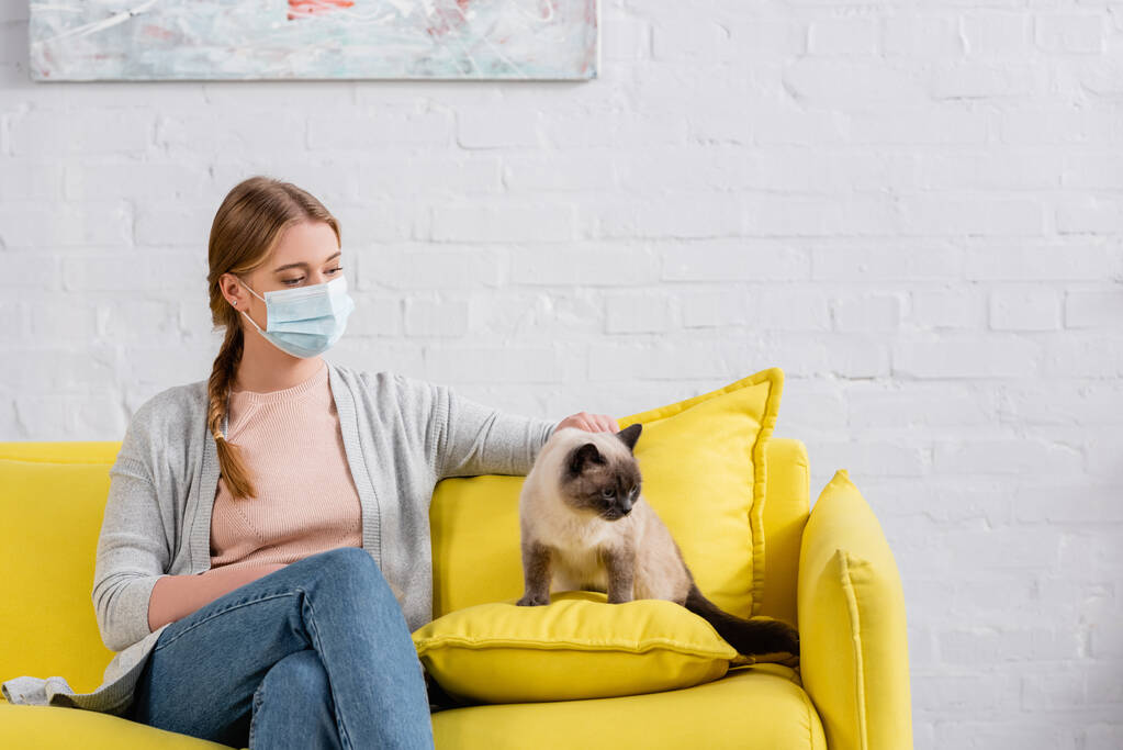 Donna in maschera medica che soffre di allergia vicino al gatto siamese  - Foto, immagini