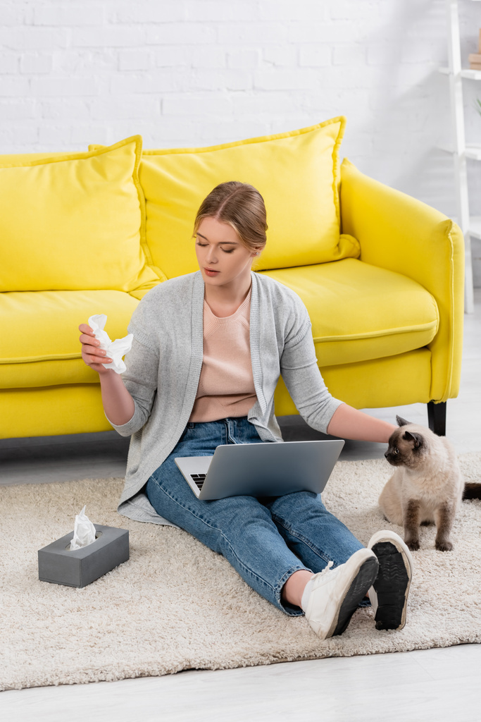 Femme avec ordinateur portable prenant serviette pendant l'allergie près du chat siamois  - Photo, image