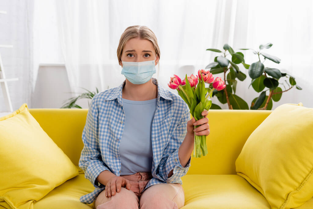 Nainen, jolla on allergia yllään lääketieteellinen naamio pitäessään tulppaanit kotona  - Valokuva, kuva