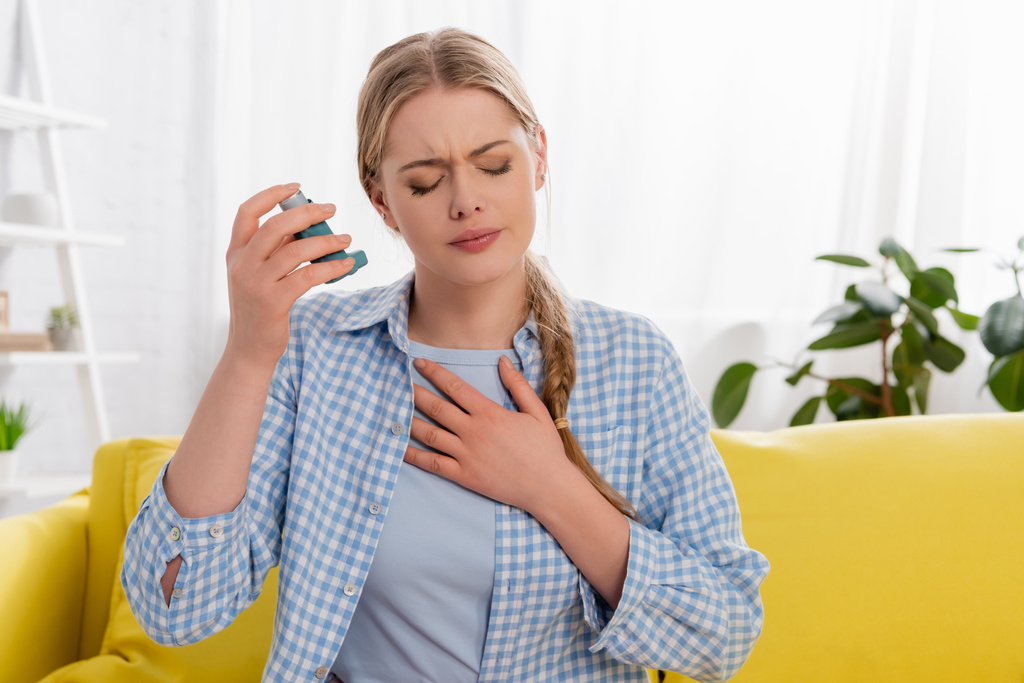 Mujer enferma con asma sosteniendo inhalador en el sofá  - Foto, Imagen