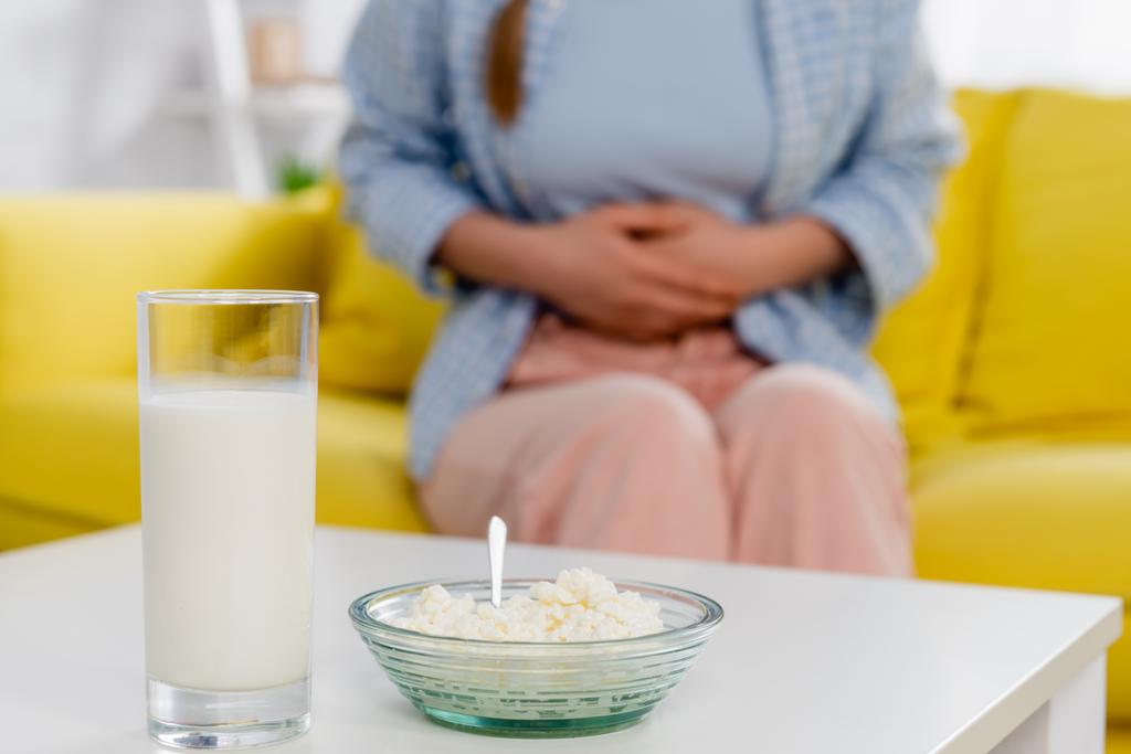 Vista cortada de queijo cottage e vidro de leite perto da mulher com alergia no fundo borrado  - Foto, Imagem