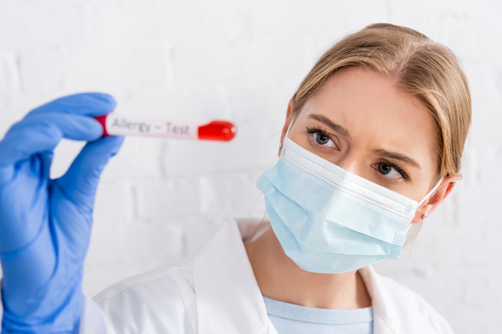 Arzt in medizinischer Maske hält Röhrchen während Allergietest auf verschwommenem Vordergrund  - Foto, Bild
