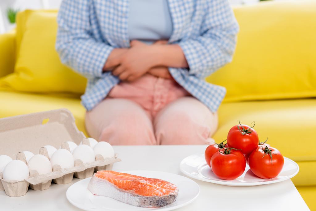Cropped view of raw salmon, tomatoes and eggs near woman with allergy on blurred background  - Foto, afbeelding