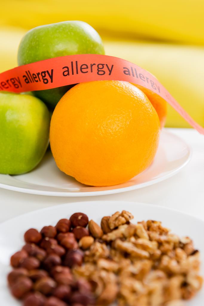 Cinta con letras de alergia cerca de frutas frescas y frutos secos en primer plano borroso  - Foto, imagen