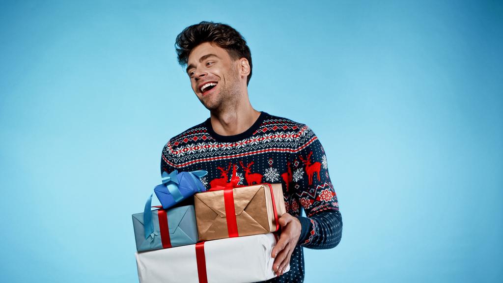 Allegro uomo in maglione che tiene regali su sfondo blu - Foto, immagini