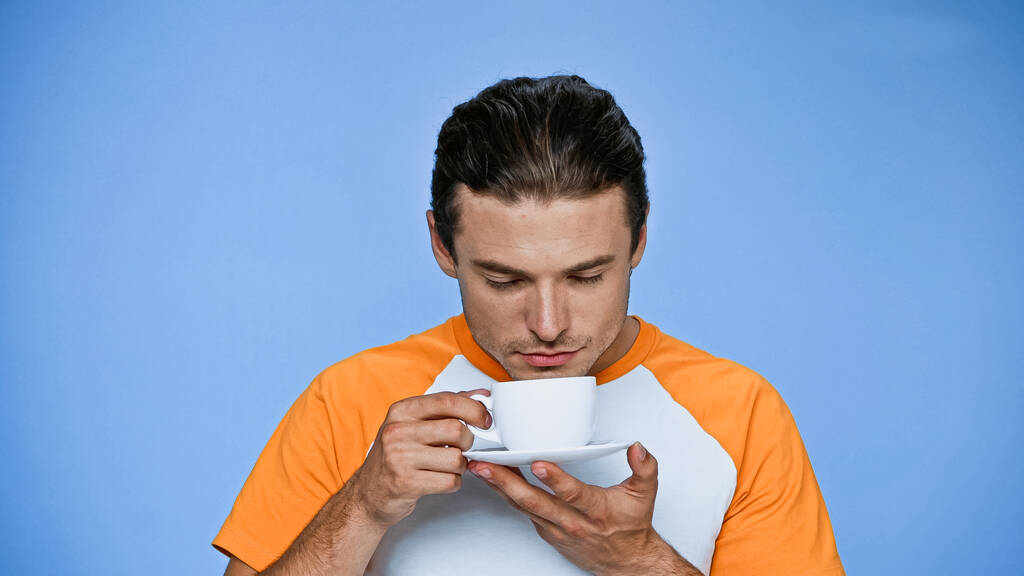 zadowolony człowiek z zamkniętymi oczami korzystających smak kawy odizolowane na niebiesko - Zdjęcie, obraz