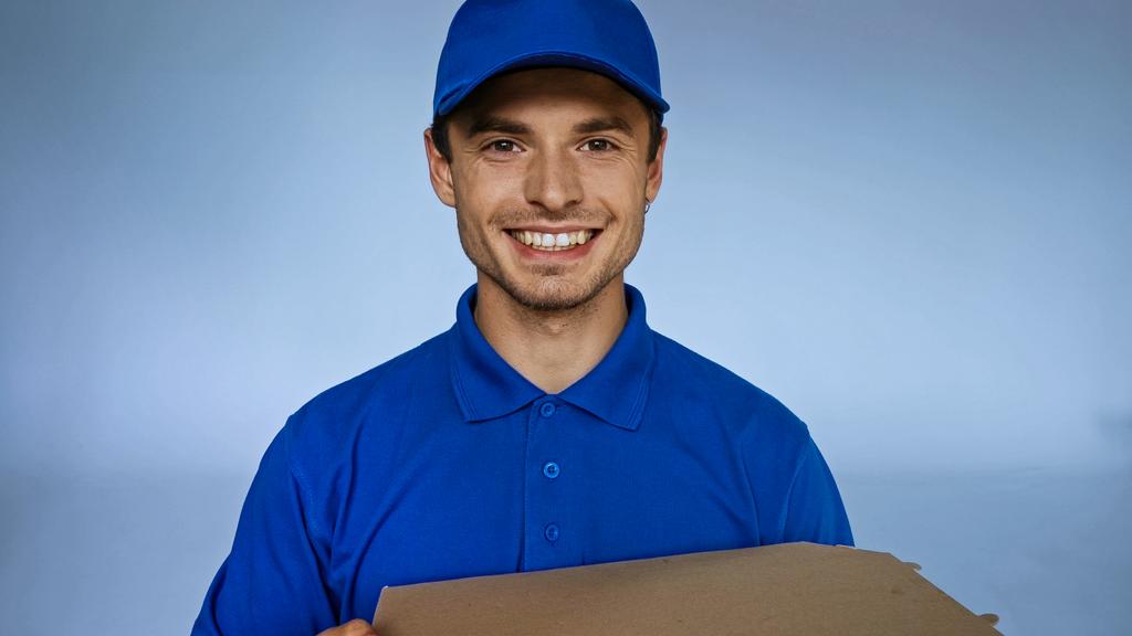 livreur gai avec boîte à pizza regardant caméra isolée sur bleu - Photo, image