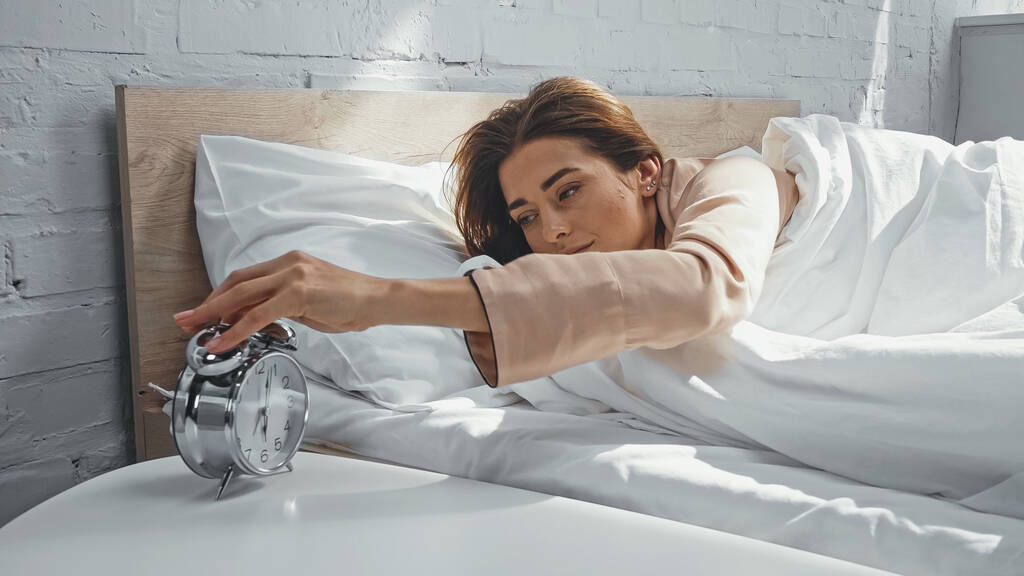 νεαρή γυναίκα κλείνει το ξυπνητήρι το πρωί - Φωτογραφία, εικόνα