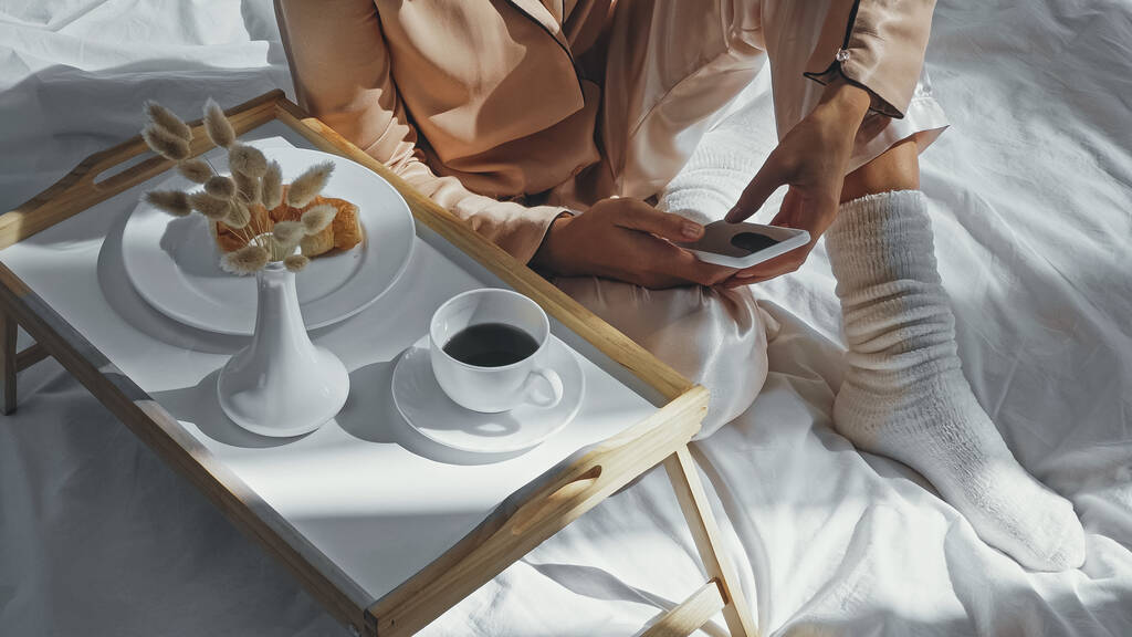 przycięty widok kobiety za pomocą smartfona w pobliżu tacy ze smacznym śniadaniem i filiżanką kawy - Zdjęcie, obraz