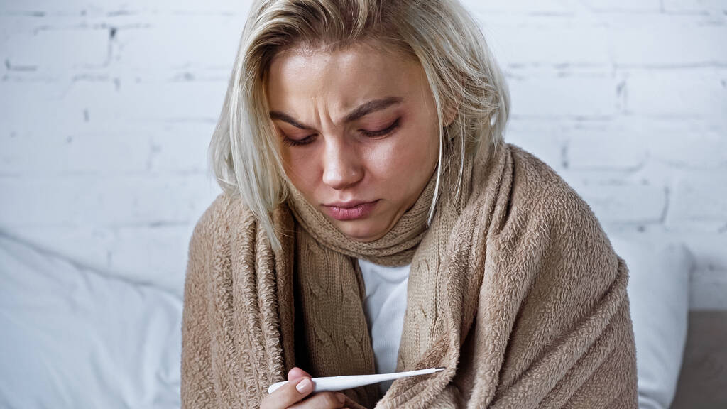 νεαρή άρρωστη γυναίκα που κοιτάζει το θερμόμετρο στην κρεβατοκάμαρα - Φωτογραφία, εικόνα