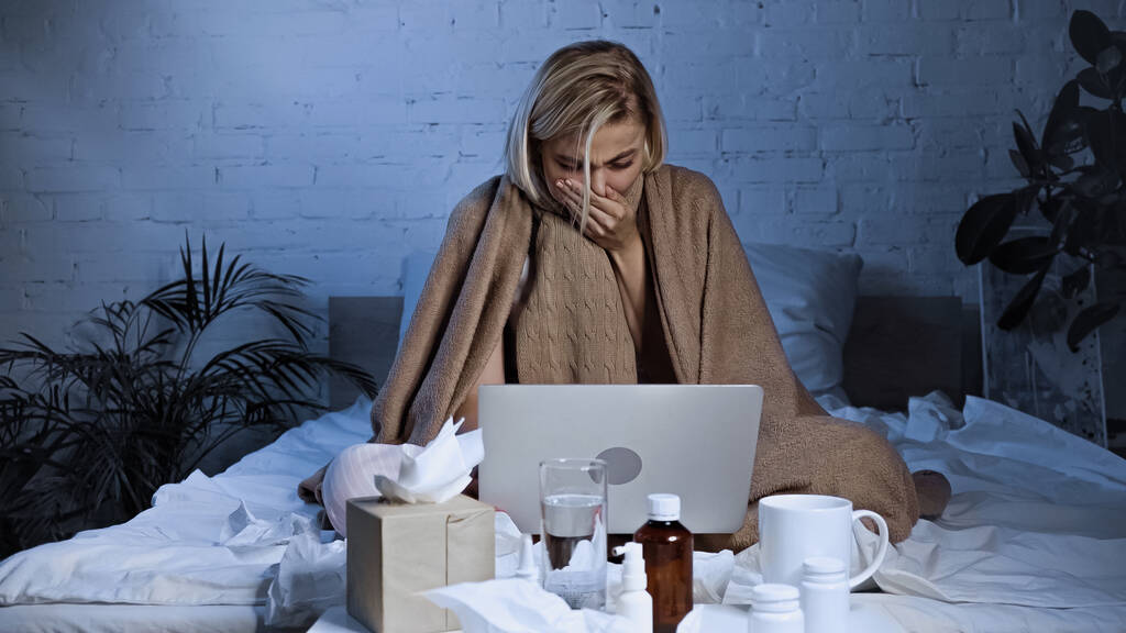 diseased freelancer sneezing near laptop and medications in bedroom - Photo, Image