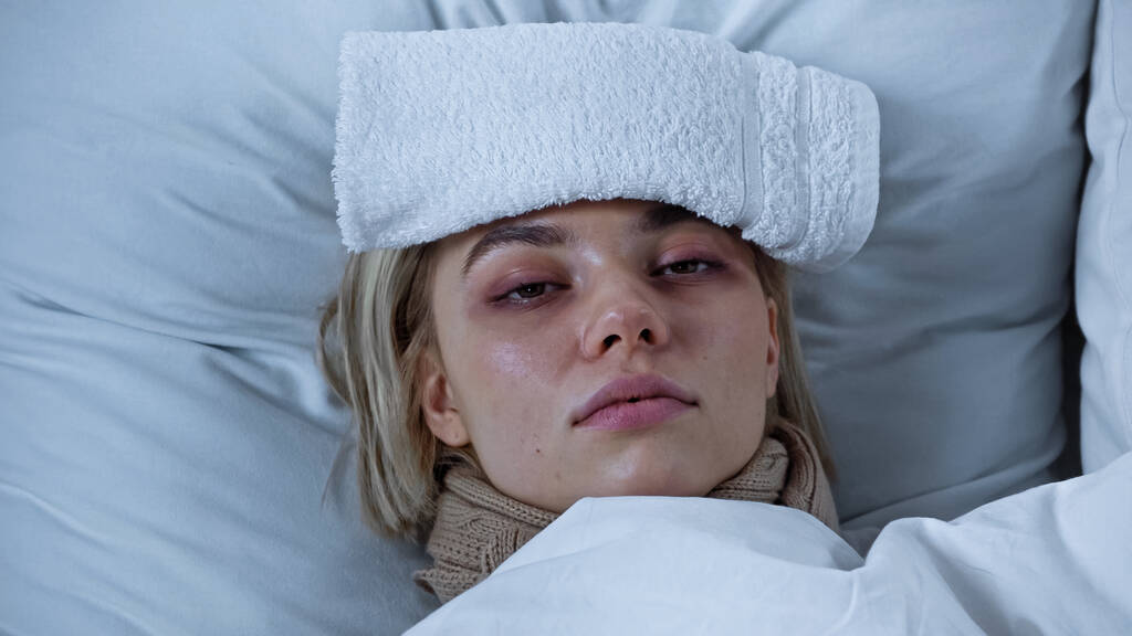 Kranke junge Frau liegt mit Handtuch auf der Stirn im Bett - Foto, Bild