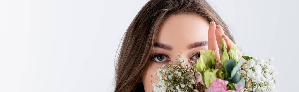 Gri pankartta izole edilmiş çiçeklerin yakınındaki kameraya bakan genç kadın görüntüsü.  - Fotoğraf, Görsel