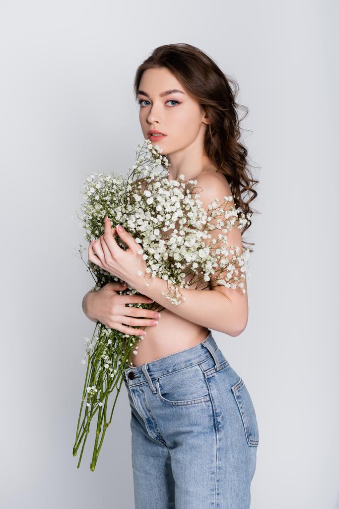 Shirtless woman holding baby breath flowers and looking at camera isolated on grey  - Photo, Image