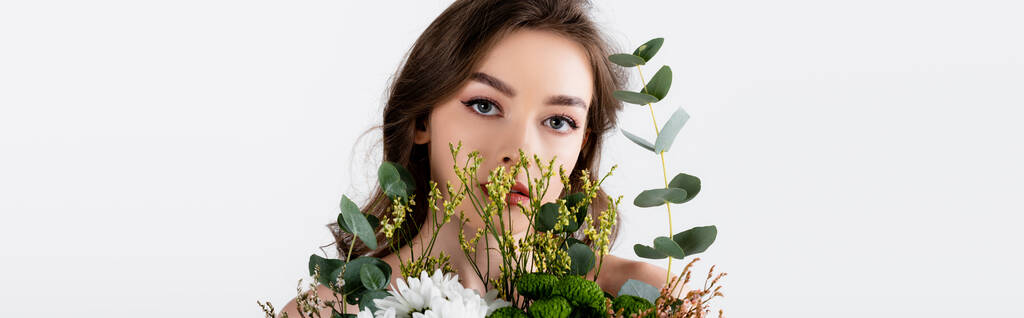 Model met naakte schouders kijken naar camera in de buurt van bloemen geïsoleerd op grijs, banner  - Foto, afbeelding