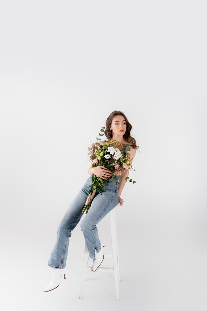 Overhemd model in schoenen en jeans met boeket op stoel op grijze achtergrond  - Foto, afbeelding