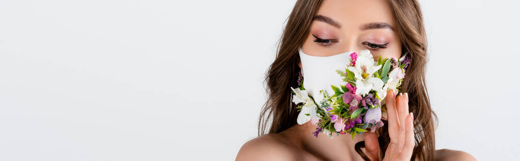 Sağlık maskesi takmış, eli çiçekli genç bir kadın, gri pankartta izole edilmiş.  - Fotoğraf, Görsel