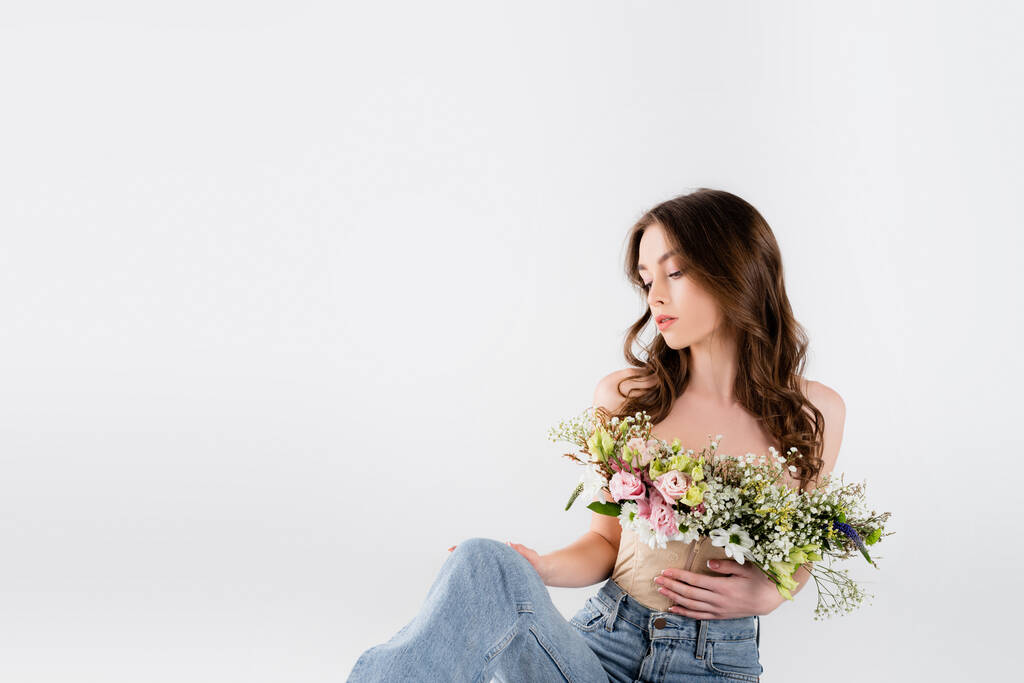 Lockige Frau mit verschiedenen Blüten in Bluse und Jeans vereinzelt auf grau  - Foto, Bild