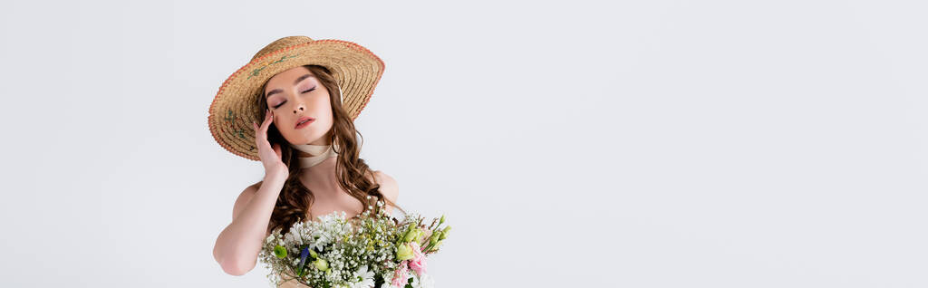 Donna in cappello di paglia in piedi con gli occhi chiusi vicino a fiori isolati su grigio, striscione  - Foto, immagini
