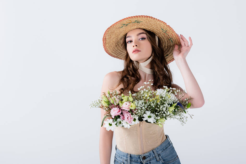 Stylish woman in straw hat with flowers looking at camera isolated on grey  - Photo, Image