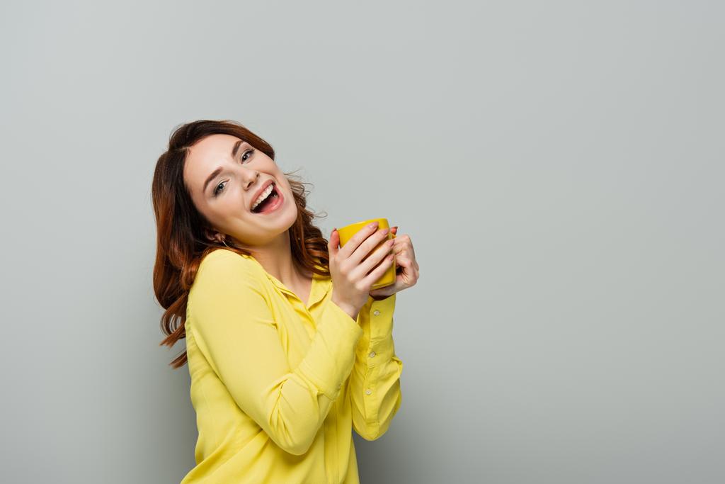 izgatott nő nézi a kamera, miközben tartja sárga csésze szürke - Fotó, kép