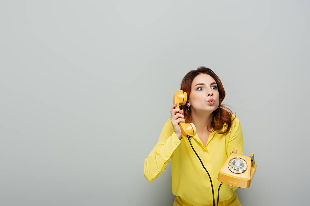 yllättynyt nainen murjottaa huulet puhuessaan vintage puhelin harmaa - Valokuva, kuva