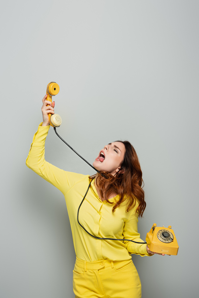 vrouw gevoel walging en steken uit tong terwijl praten vintage telefoon op grijs - Foto, afbeelding