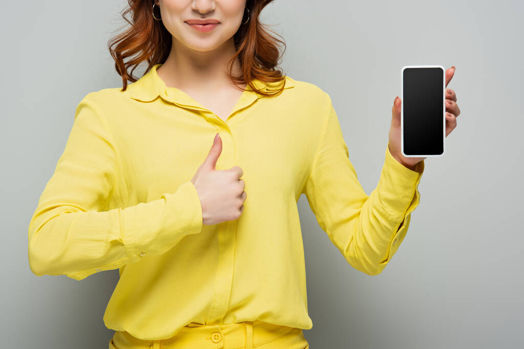 partial view of smiling woman holding smartphone with blank screen and showing like on grey - Photo, Image