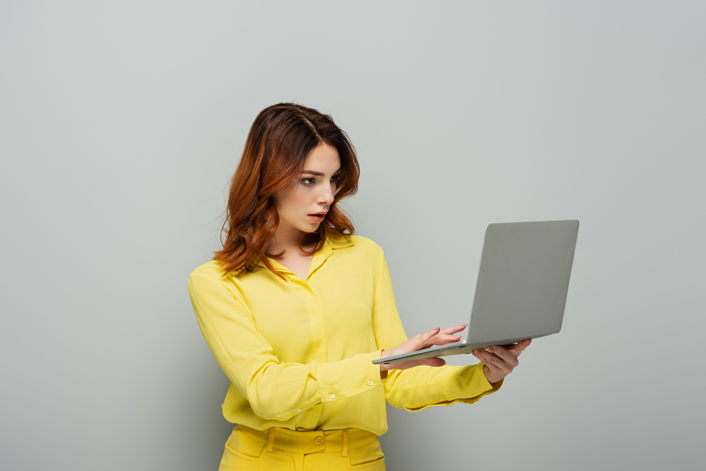 Geballte Frau in gelber Bluse tippt auf Laptop auf grau - Foto, Bild