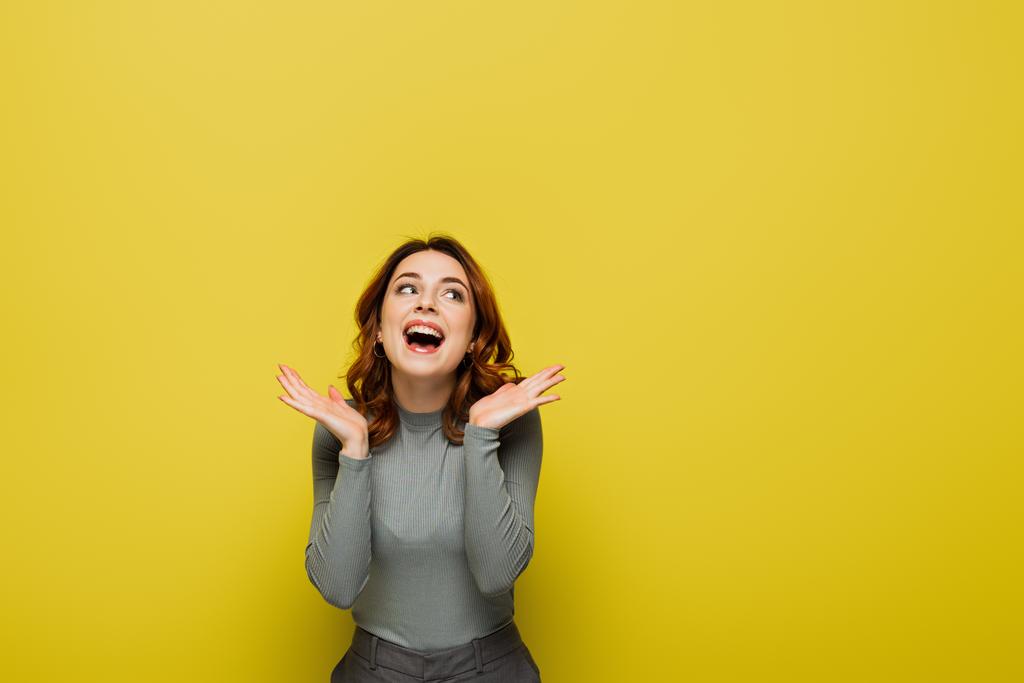 boldog nő hullámos hajjal néz félre, miközben áll nyitott tenyérrel sárga - Fotó, kép