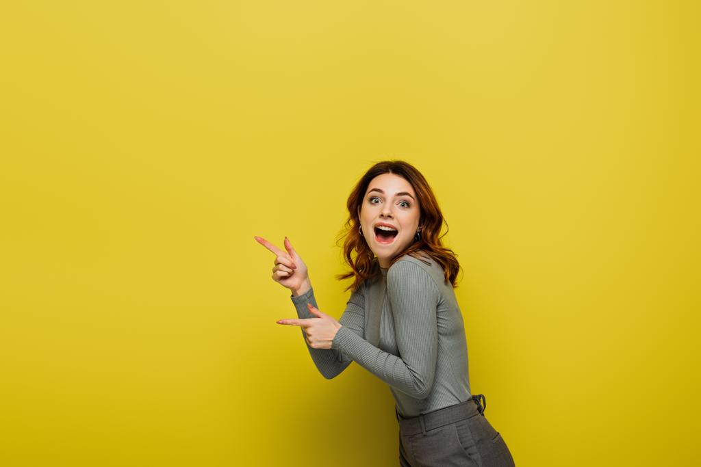 zdumiona kobieta wskazująca palcami podczas patrzenia na żółty aparat fotograficzny - Zdjęcie, obraz