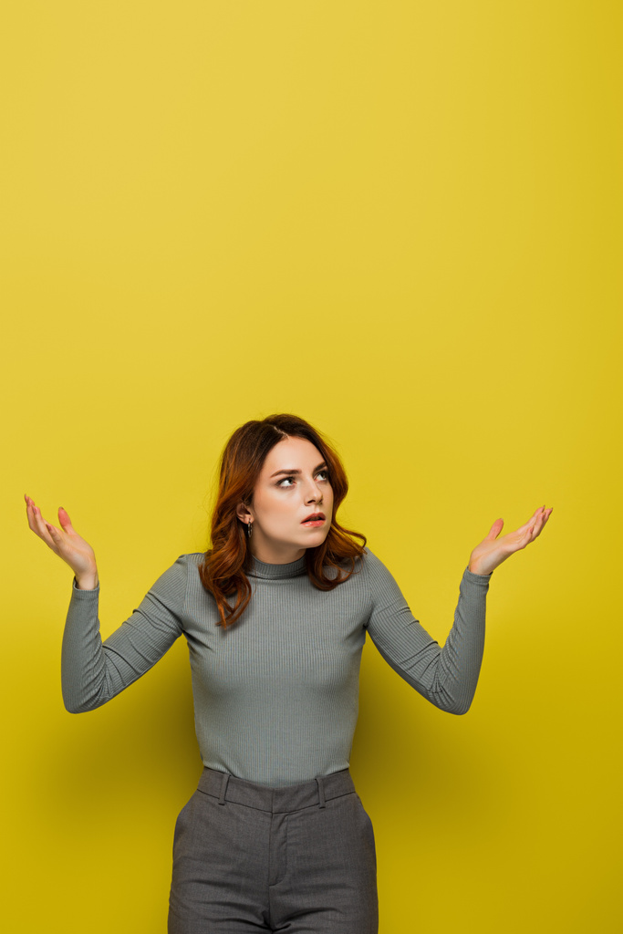 mujer disgustada con el pelo rizado mirando hacia otro lado mientras está de pie con los brazos abiertos en amarillo - Foto, Imagen