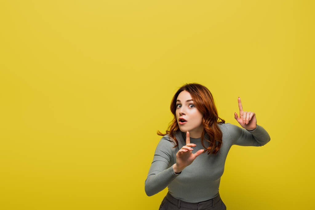 woman with curly hair and open mouth pointing with fingers isolated on yellow - Photo, Image
