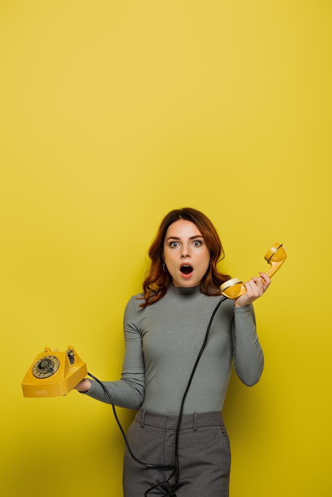 σοκαρισμένη νεαρή γυναίκα εκμετάλλευση ρετρό τηλέφωνο απομονώνονται σε κίτρινο - Φωτογραφία, εικόνα