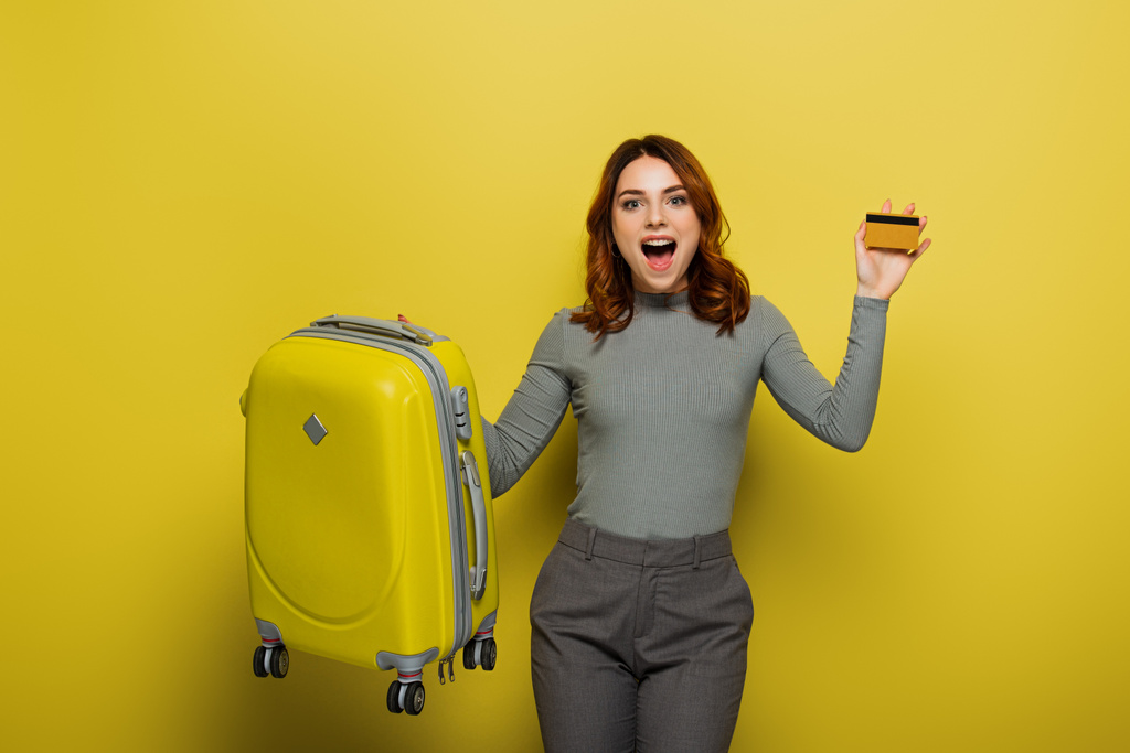 zdumiona kobieta z kręconymi włosami bagażu i karty kredytowej na żółty - Zdjęcie, obraz