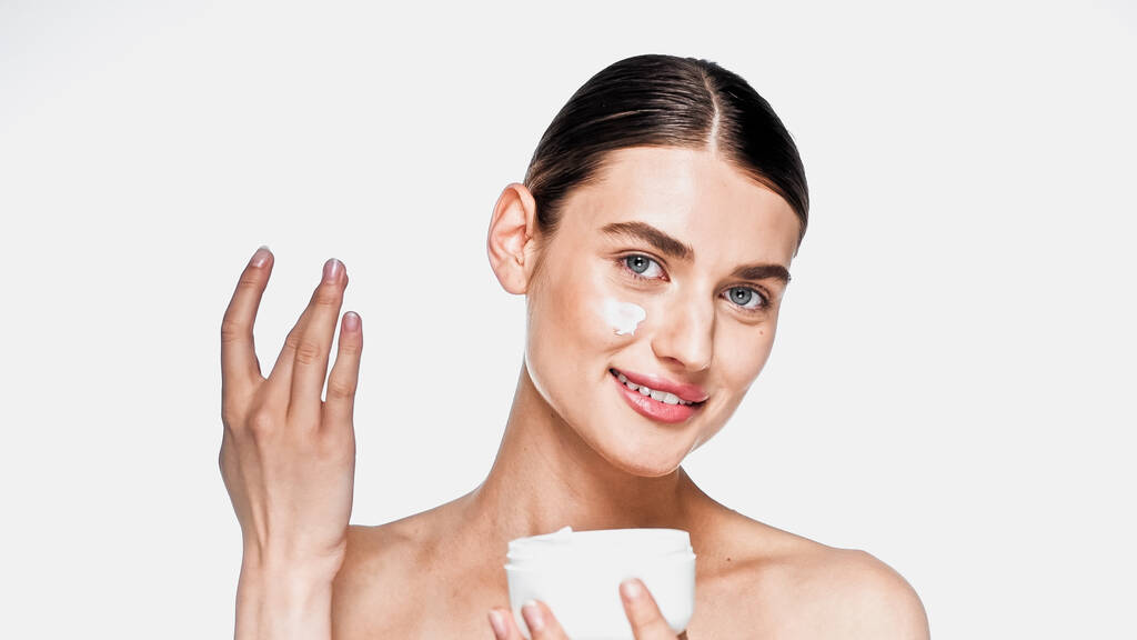 šťastná žena drží sklenici a použití kosmetické krém izolované na bílém - Fotografie, Obrázek