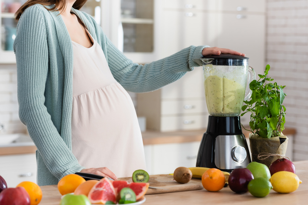 vue partielle de la femme enceinte préparant smoothie aux fruits au mélangeur - Photo, image