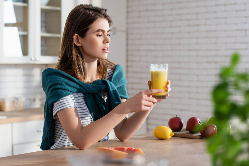 young woman holding glass of juice near fresh fruits on blurred foreground - Photo, Image