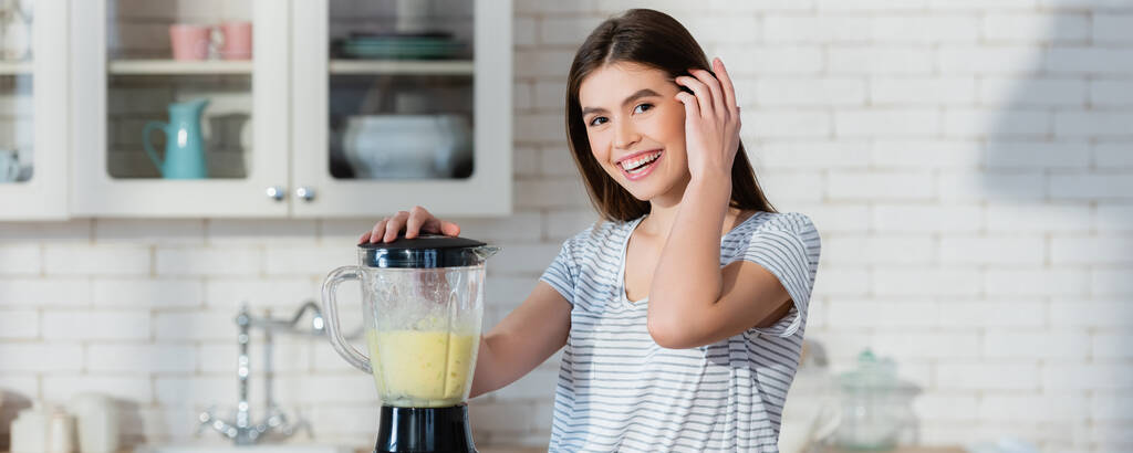 femme heureuse fixant les cheveux tout en préparant le smoothie dans le mélangeur, bannière - Photo, image