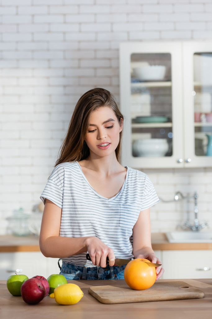 mujer joven corte naranja mientras prepara el desayuno en la cocina - Foto, Imagen