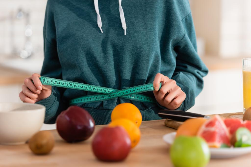 vista cortada da mulher que mede a cintura perto de frutas frescas em primeiro plano borrado - Foto, Imagem
